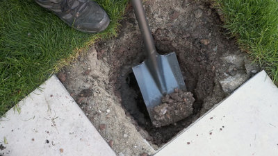 Person using a narrow shovel to dig a circular hole ready to fit a post.
