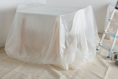 A room prepared for paint removal, with a table covered in a plastic dust sheet and additional dust sheets protecting the floor.