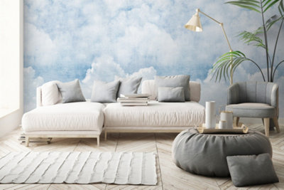 A living room with a blue and white cloudy sky wallpaper mural feature wall, a white sofa and light wooden flooring.