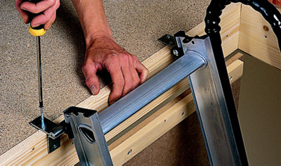 Securing a loft ladder hinge to the edge of a loft hatch using a screwdriver.