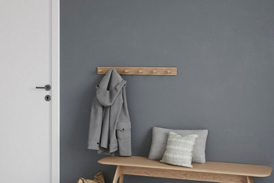 Wooden bench with cushions and a rack with a grey coat against a dark grey wall and white door.
