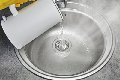 Pouring boiling water from a kettle straight down the plughole of a kitchen sink.
