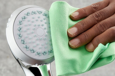 Using a microfibre cloth to clean the nozzles on a hand held shower head.