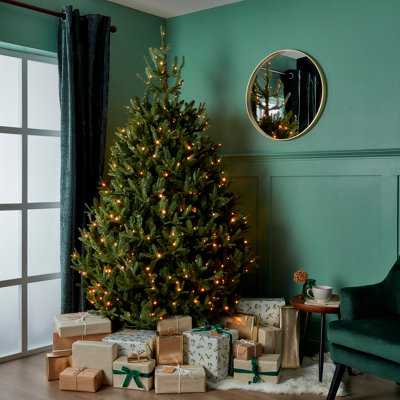 Artificial, natural effect, pre-lit tree tree in a room, with the skirt area surrounded by gifts.