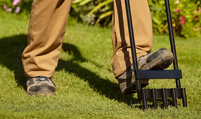 Person placing their foot onto the top of a lawn aerator to push it into the grass.