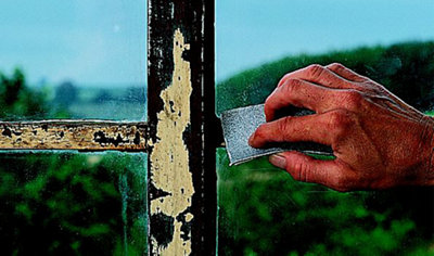 Using a piece of sandpaper to sand down a metal window frame.