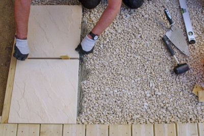 Person wearing gloves placing a second wood spacer in the gap between two paving slabs that have been laid on top of mortar.