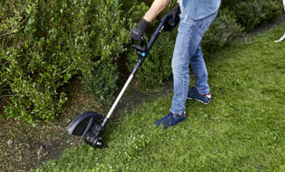 A person trimming the edge of a lawn using a strimmer.