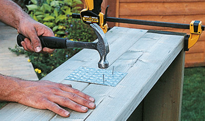 Person using a hammer and nails to secure a metal plate to two deck joists to join them together.