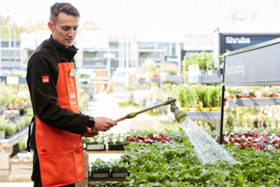 A B&Q colleague in a B&Q garden centre watering the plants using a hose with a sprinkler head.