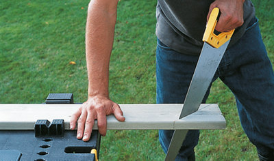 Person using a saw to cut a diagonal line in a piece of timber which is sat on a workbench.
