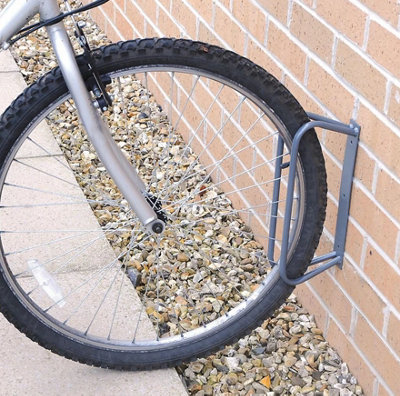 A wall mounted wheel holder attached to a brick wall with a bike stored in it.