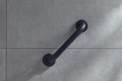 Matt black grab rail installed diagonally on grey tiled wall.