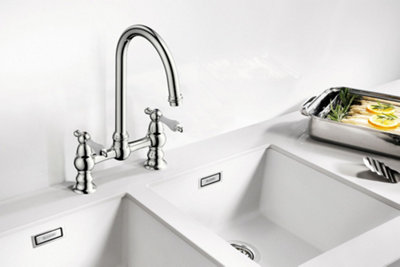 Cooke & Lewis Sherrard chrome effect kitchen deck bridge tap installed on top of a white undermount two bowl kitchen sink.