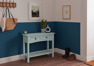 A light blue cabinet standing in the hallway next to a rack on which a bag hangs and shoes arranged against a dark blue and white wall on which pictures hang.