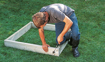 Person using a hammer to drive a nail into a deck joist to complete a square made from deck joists.