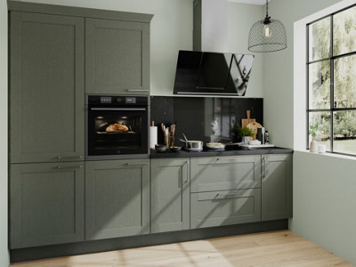 Galley kitchen with green cabinets, black worktops, light green walls and light laminate wood flooring.