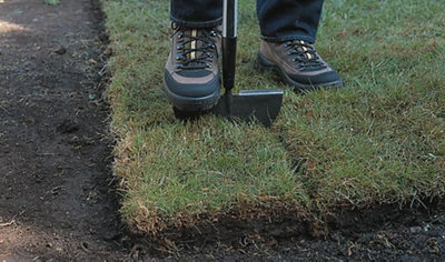 Person placing their foot on the top of a lawn edging tool to push it into the ground.