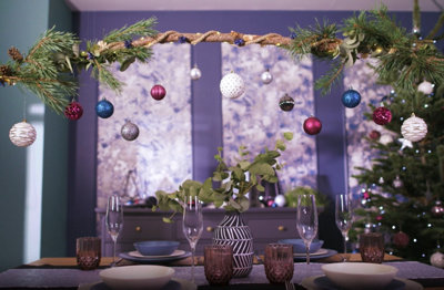 Assorted blue, pink, silver and white baubles hanging from a festive branch above a dining table.