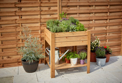 A small, raised timber planter with four legs and a storage shelf underneath.