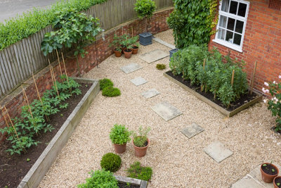 Gravel front garden with square stepping stone slabs leading round the side of the house.
