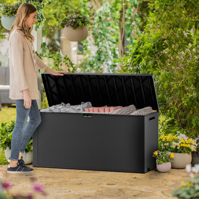 Person lifting the lid of a large plastic garden storage box which has garden cushions and blankets inside.