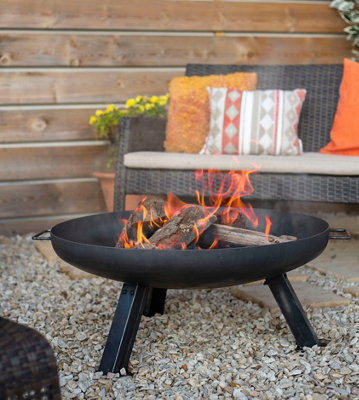 Black fire pit filled with lit fire wood, casting a warm glow throughout the garden.