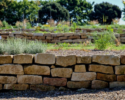 Sloped garden transformed with rustic stone walls, creating tiered levels and turning uneven terrain into a functional, visually stunning outdoor space.