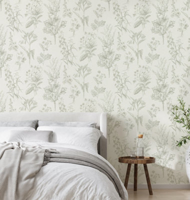 Green and white floral wallpaper in bedroom with a grey bed with white bedding and a dark wooden bedside table.