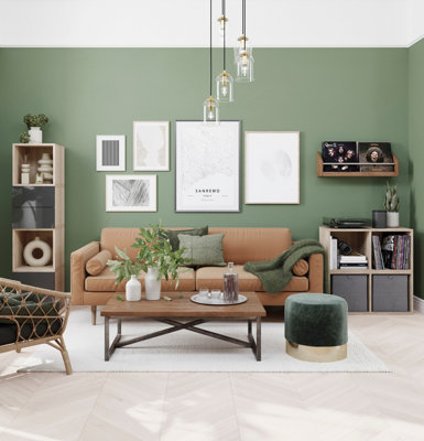 Green living room with gallery wall behind a tan leather sofa.