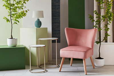 A green living room with a pink statement chair and a variety of houseplants.