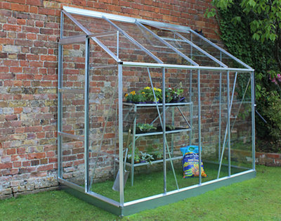 A lean-to greenhouse with a pitched roof placed against the brick wall of a house.