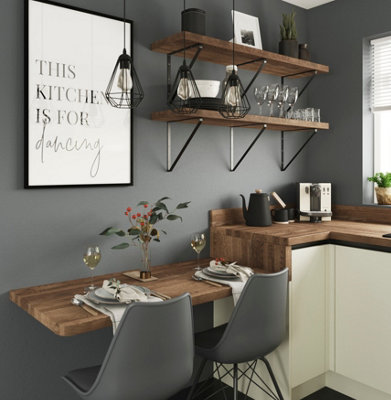 Grey kitchen with dark wood worktops and shelving, with a low breakfast bar and grey chairs.