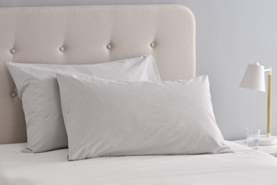 Two pillows stacked on top of each other, leaning against the fabric headboard of a bed.