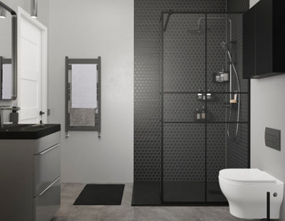 Walk in shower with black shower tray, black frame shower screen, black geometric tiled walls and chrome mixer shower. Shower is installed in grey bathroom with grey tiled flooring and grey walls.