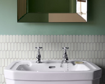 Bathroom sink set against a half tiled wall with scalloped white tiles and green painted upper walls.