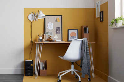 A home office zoned with yellow paint on the walls and floors, with a wooden desk with white legs and a white office chair.