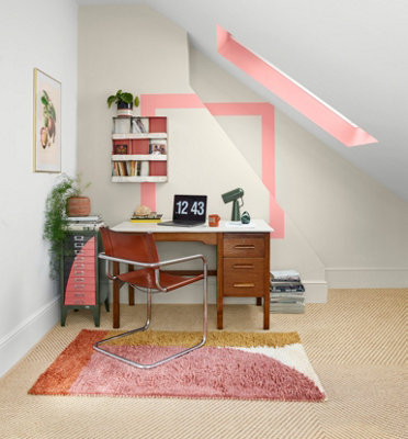 A home office featuring a striking coral pink square feature on the walls, with the vibrant colour extending to the roof window casing and shelves, creating a unique and playful design.