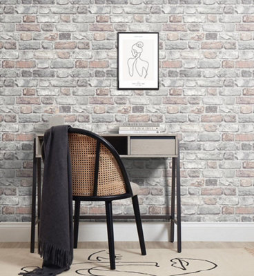 A home office with a light grey and black desk, a black rattan chair and light grey brick wallpaper.