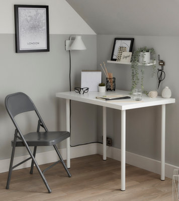 A white and grey home office with a white desk, grey folding chair and a white wall mounted light.