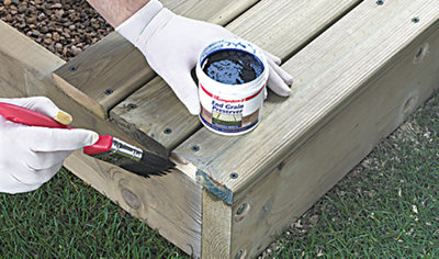 Person wearing gloves using a paintbrush to apply end grain preserver to the end of a decking board that has just been installed.