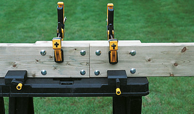 Two sections of deck board placed on top of a work bench are clamped together using two clamps.