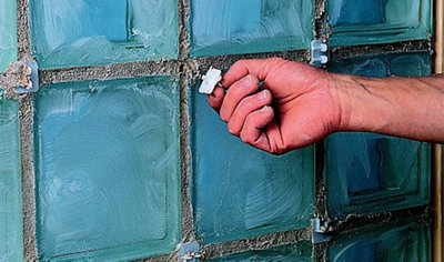 Person removing the tab from a spacer that is sat in the mortar of a glass block wall.