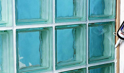 Using a sealant gun to apply silicone sealant to the joints in a glass block wall to leave behind a smooth finish.