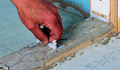 Person laying a glass block wall spacer on top of a mortar bed on the floor. Another spacer has been installed against the wall where the first block will be laid.