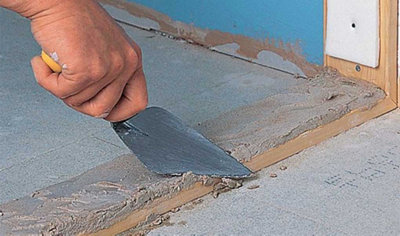 Person using a trowel to lay a bed of mortar on top of a piece of timber that's sat on the floor.