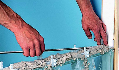 Person laying a steel reinforcing bar on top of mortar that's sat on top of an unfinished glass block wall.