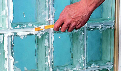 Person using a striking tool to compact the panel grout that has been applied to the joints of a glass block wall.