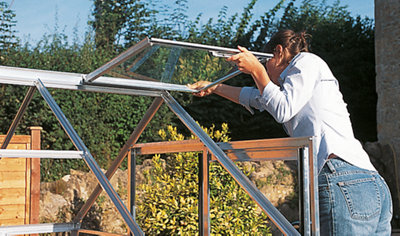 Person securing a greenhouse roof vent to a completed greenhouse frame.