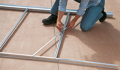 Person fitting two sections of a metal greenhouse frame together on the floor.